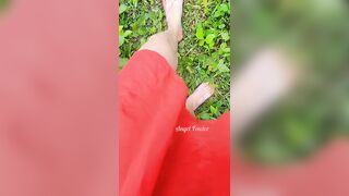 Village woman in a red tunic is pissing in the middle of a green field