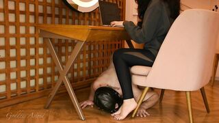 Slave serves as footstool on all his fours while Goddess is on laptop